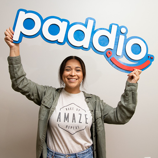 paddio employees smiling and holding up paddio logo sign